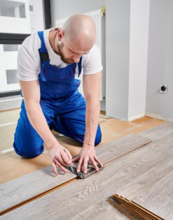 Skilled flooring installer laying hardwood planks on a wooden floor for a professional finish.
