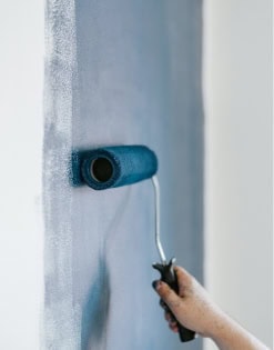 A person applying fresh paint to a wall using a paint roller, showcasing home improvement and interior decorating skills.