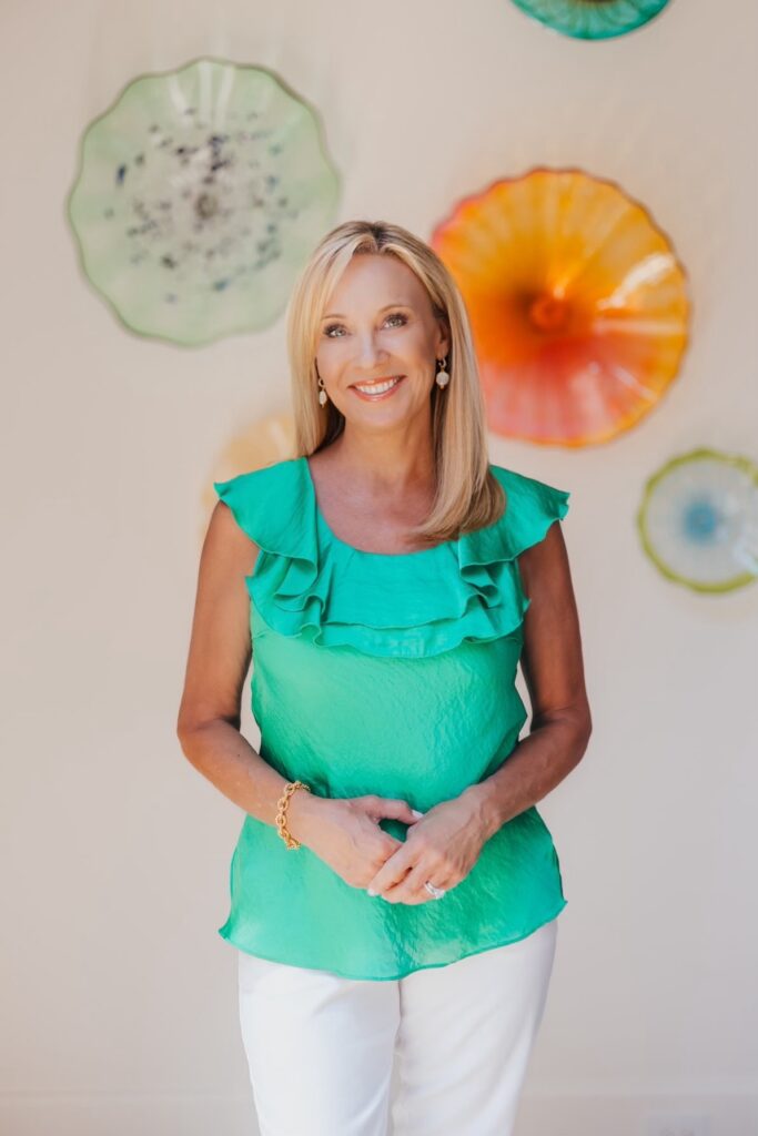 Elegant woman smiling in a vibrant green ruffled top, standing against a colorful glass art backdrop, showcasing confidence and style.